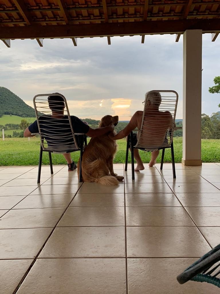 Duas pessoas e o golden na varanda assistindo ao pôr do sol