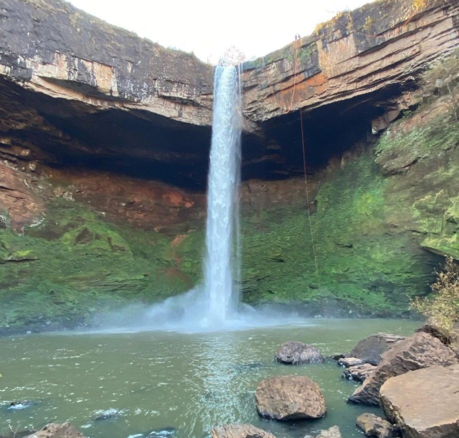 Cachoeira alta caindo em um poço de água esverdeada entre paredões de pedra