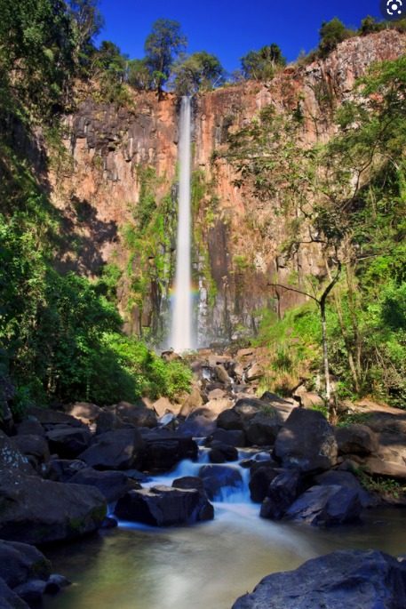 Cachoeira alta com arco-íris entre as pedras e a mata